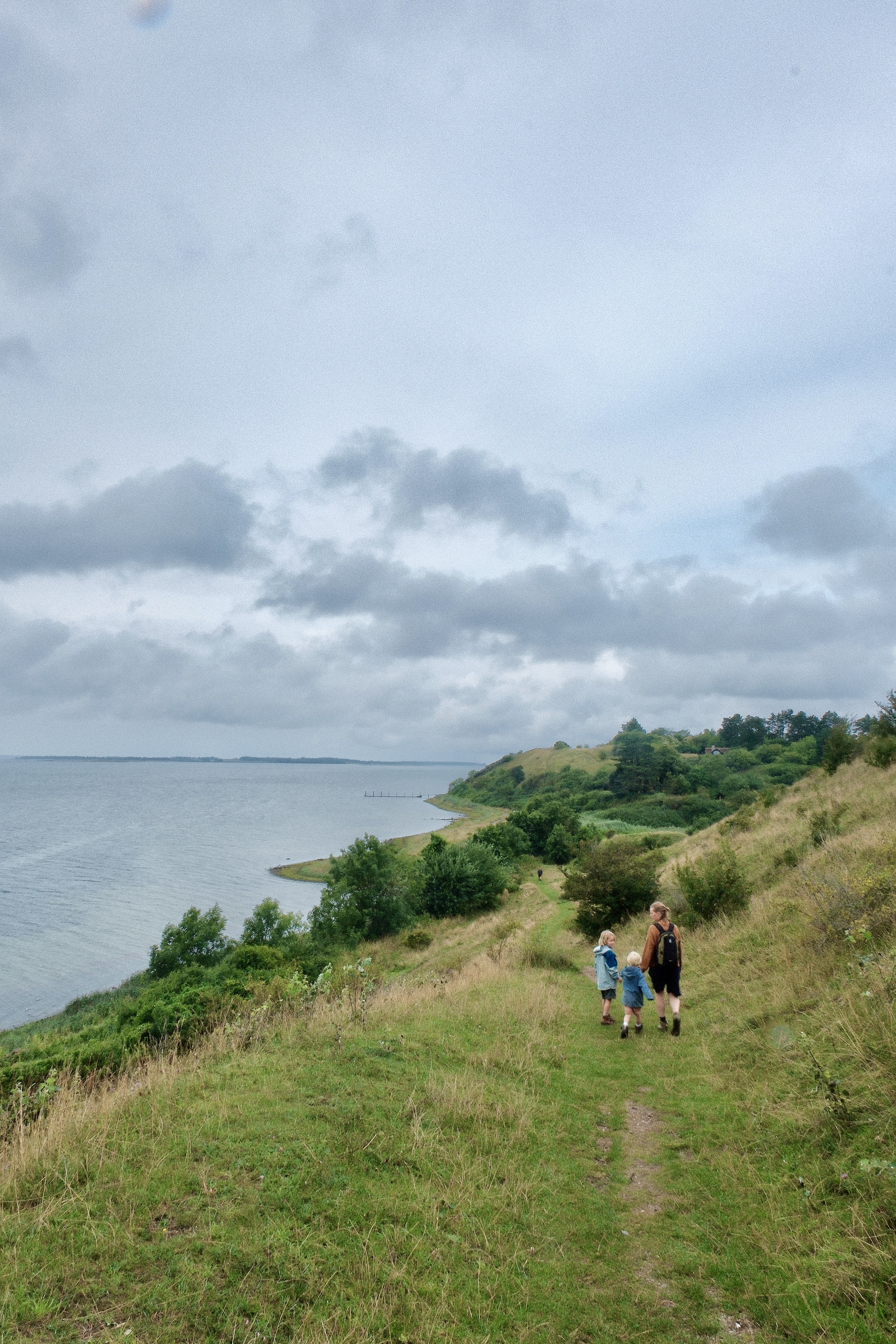 Familie på vandretur langs stien i Ejby Ådal med udsigt over kystlandskab, grønne skråninger og fjorden.