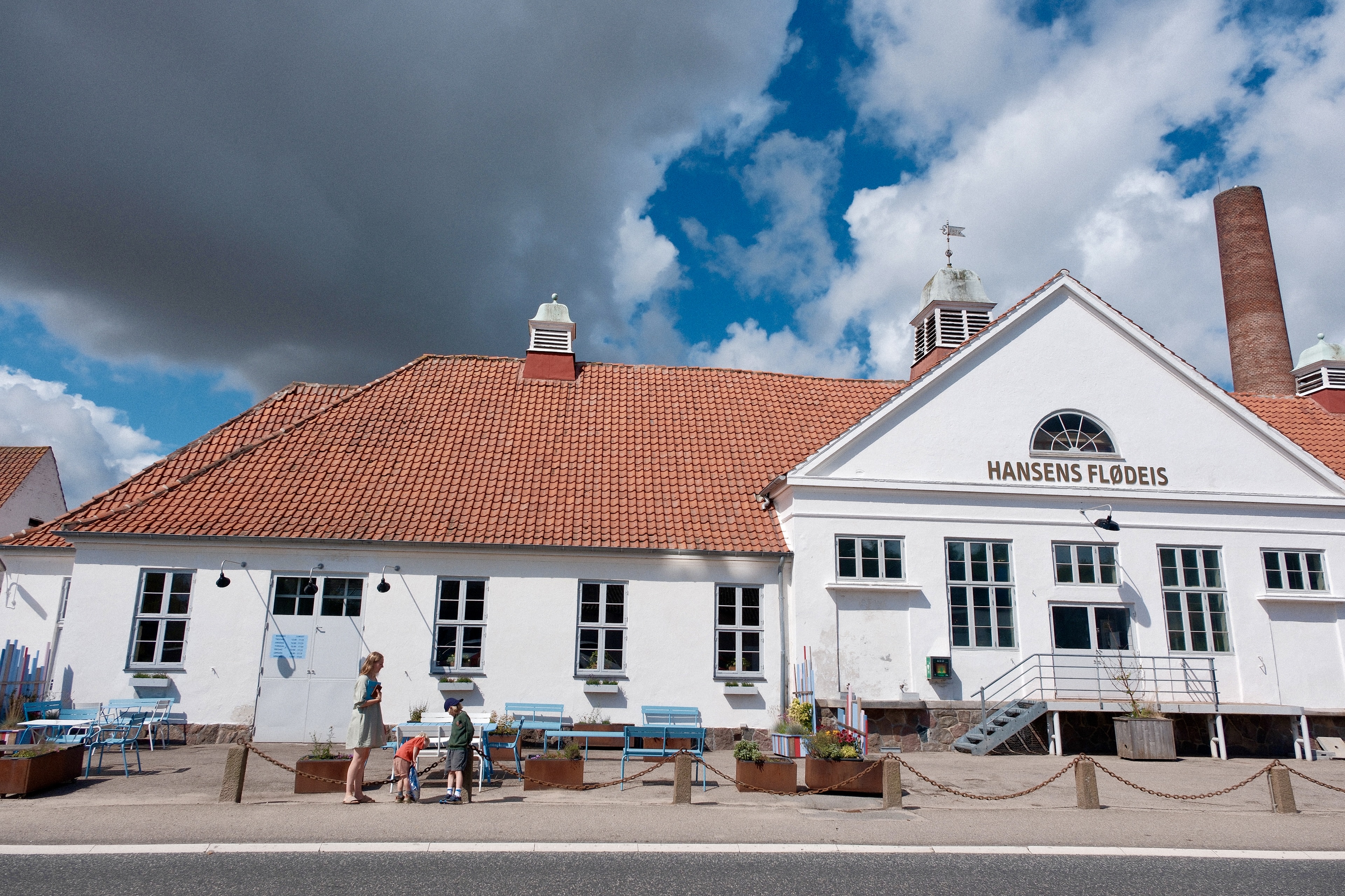 Facaden på Hansens Is Café med udendørs siddepladser foran den historiske bygning under blå himmel.