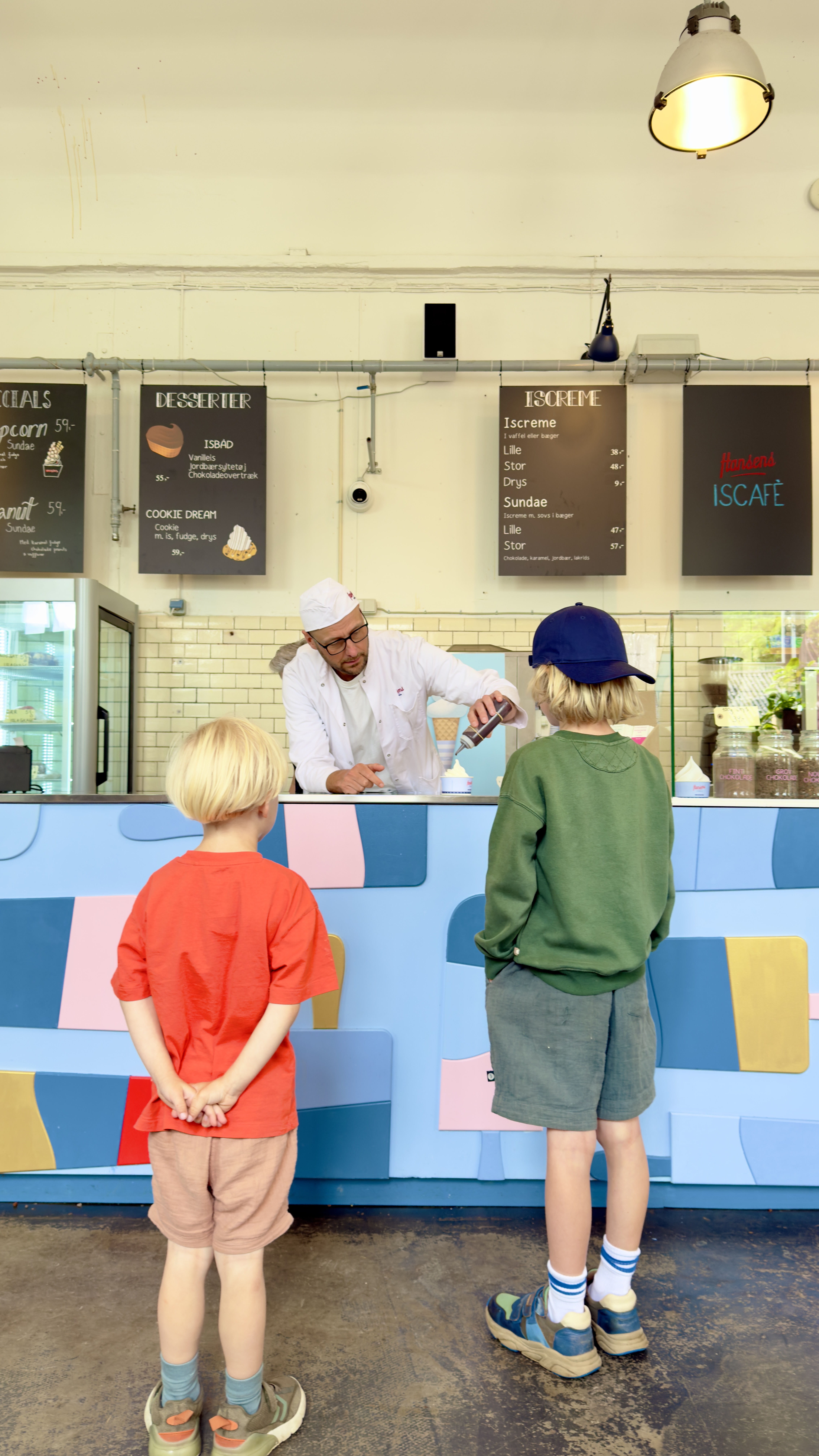 To børn ser på, mens en medarbejder serverer frisklavet is ved disken hos Hansens Is Café.