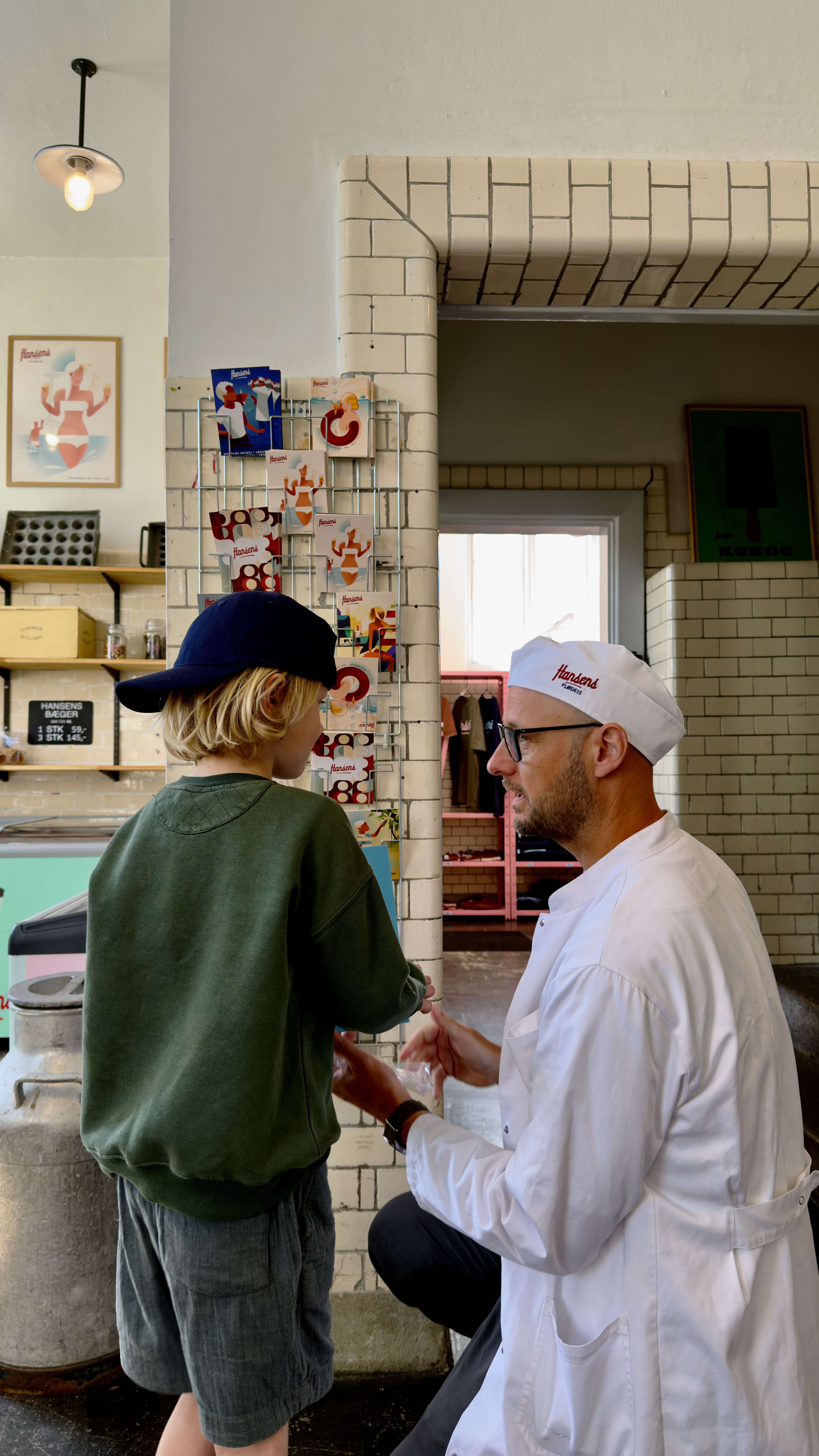 Barn taler med en medarbejder fra Hansens Is Café i den hyggelige café omgivet af isprodukter og interiør i retrostil.