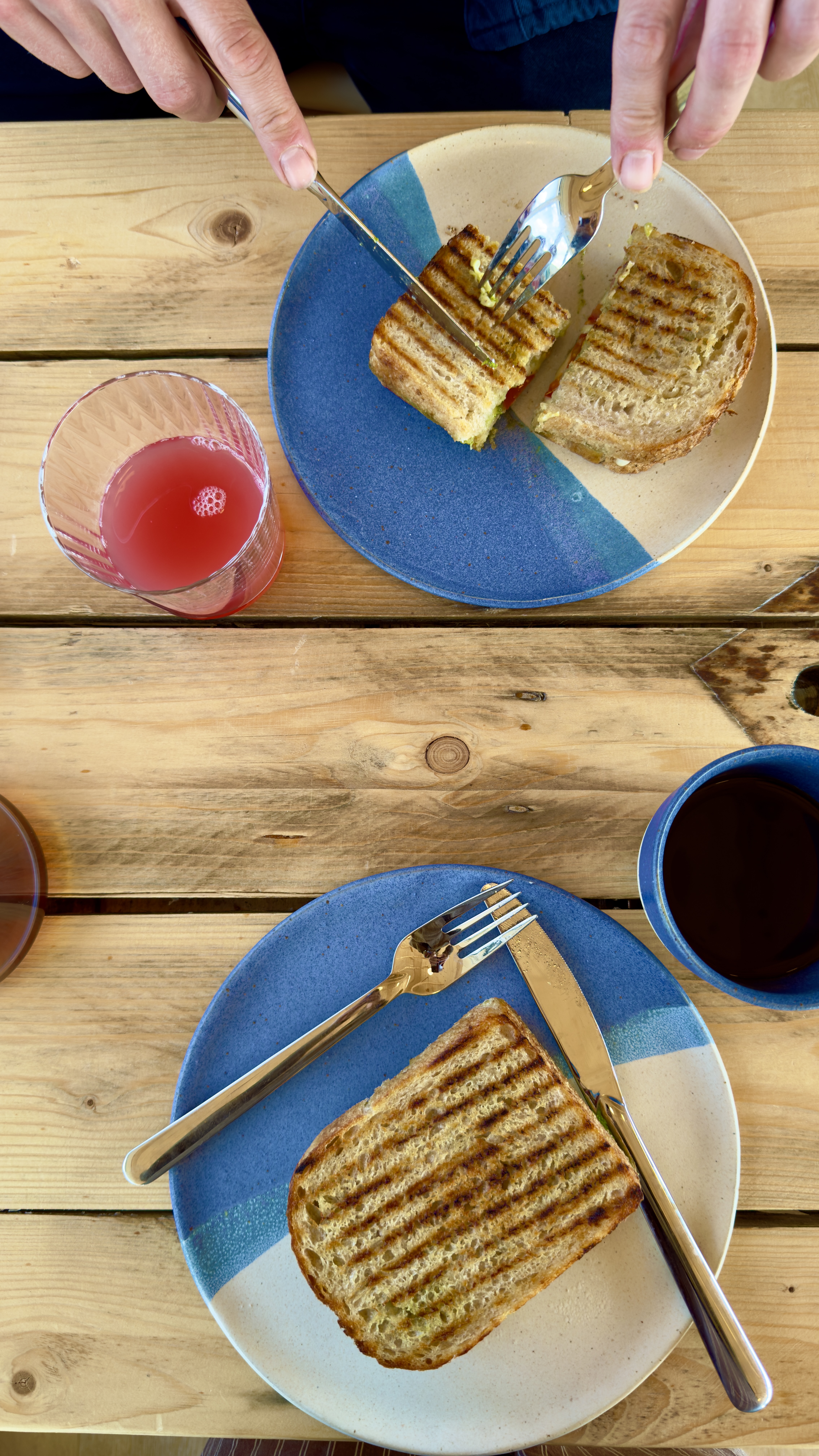 Servering med grillede sandwiches og drikkevarer på træbord hos SeaLevel Kaffebar.