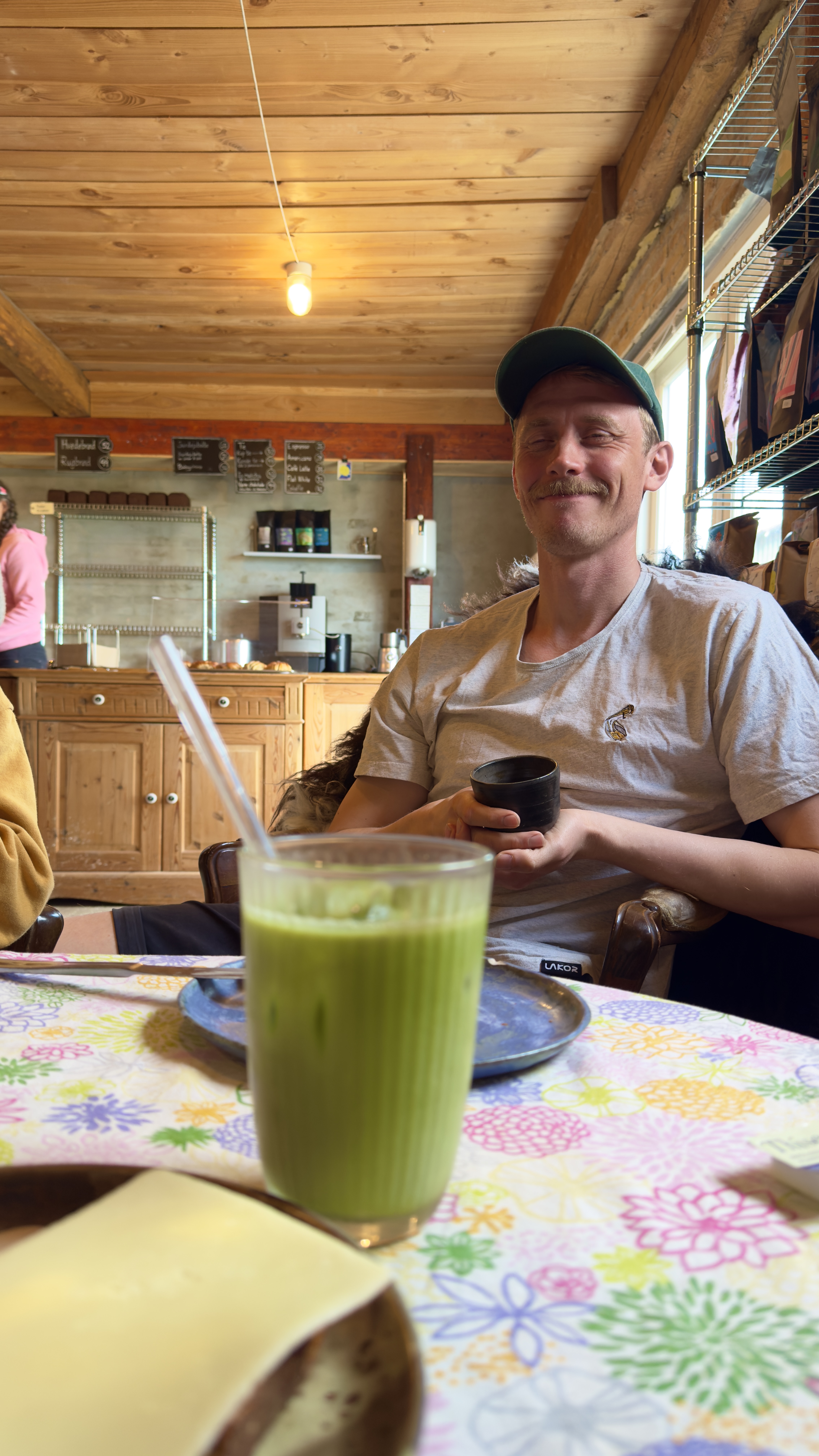 Gæst nyder en grøn økologisk drik i den rustikke gårdcafé hos Hegnsholt Økologisk Landbrug og Gårdbutik.