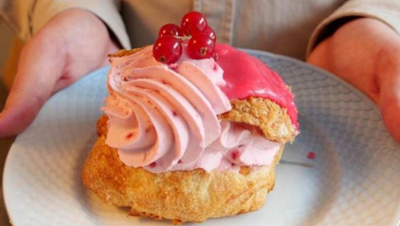 En person holder en tallerken med en fastelavnsbolle med lyserød creme og ribs på toppen.