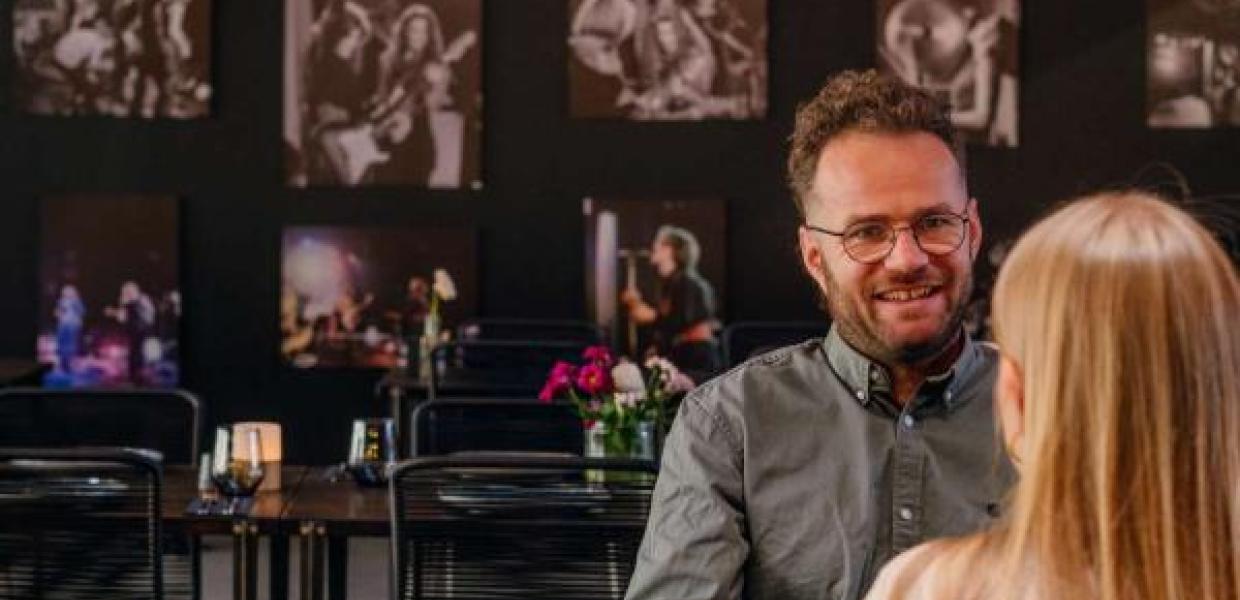 To personer sidder ved et bord i Ragnarocks café, omgivet af vægge dekoreret med rockkoncertbilleder.