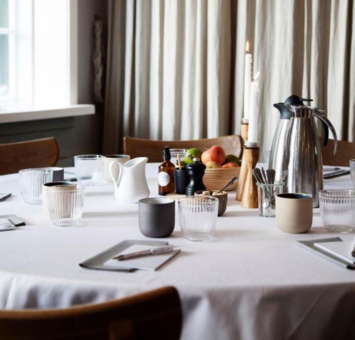 Opdækket mødebord i Herthadalen med kaffekande, glas, keramikkrus, frugtskål og blokke til notater.